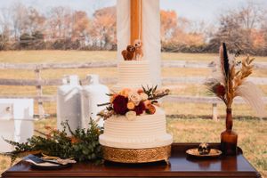 Wedding cake and floral decorations displayed on wooden table at outdoor reception.
