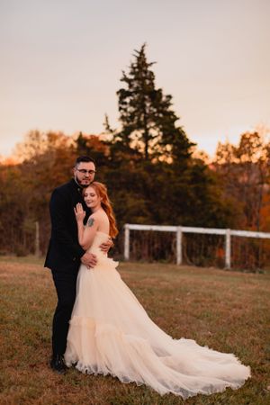 Elegant wedding couple poses in field at sunset with flowing white dress.