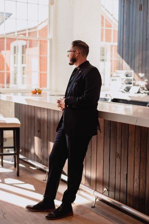 A person in black formal attire stands by a window in an indoor venue.