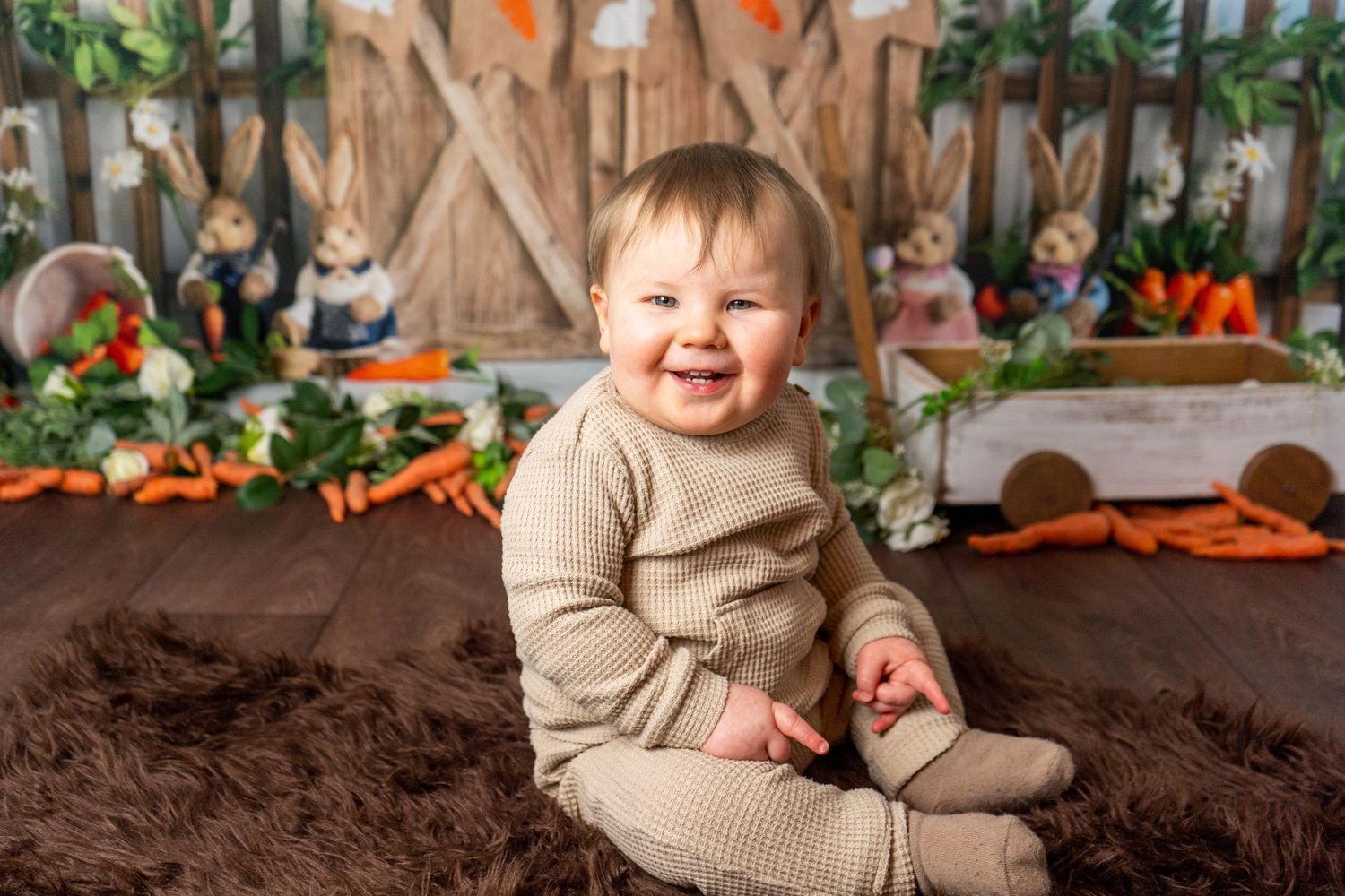 baby boy smiling sat on a brown rug for easter session with rabbits by client of heather katie photography.