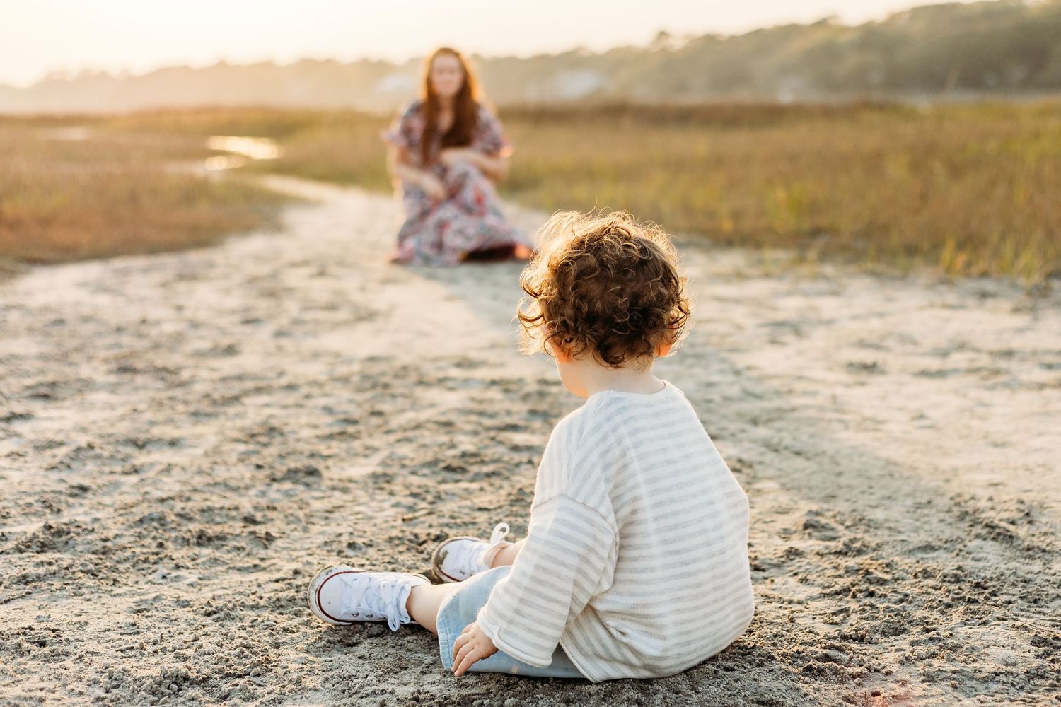 A child in white sitting on a sandy path at golden hour.