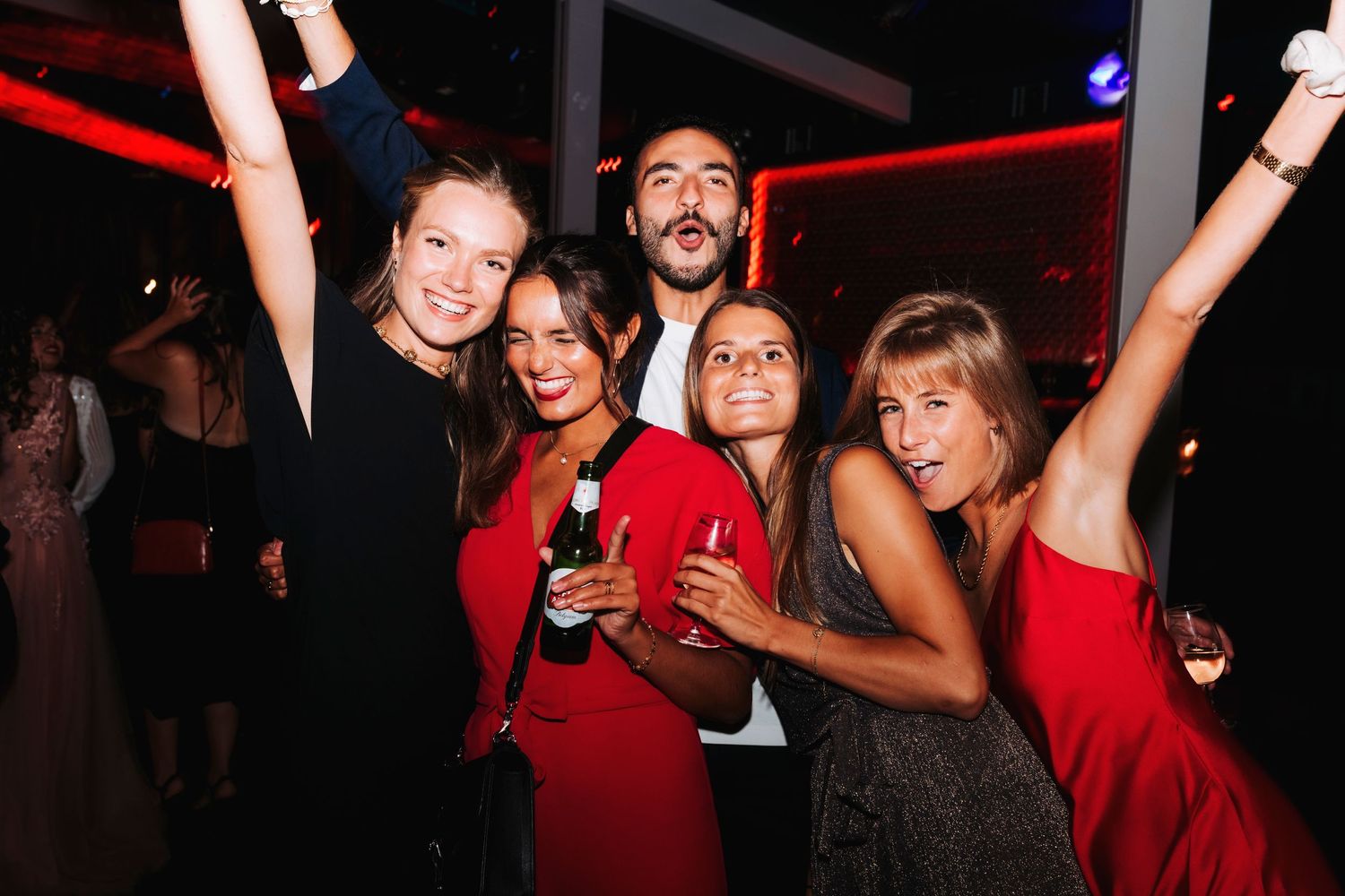 Group of friends dancing and celebrating at nightclub with red lighting.