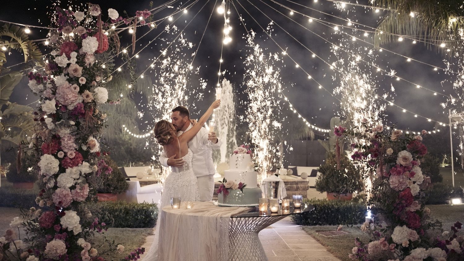 Wedding reception setup with twinkling lights, floral arches, and celebratory sparklers.