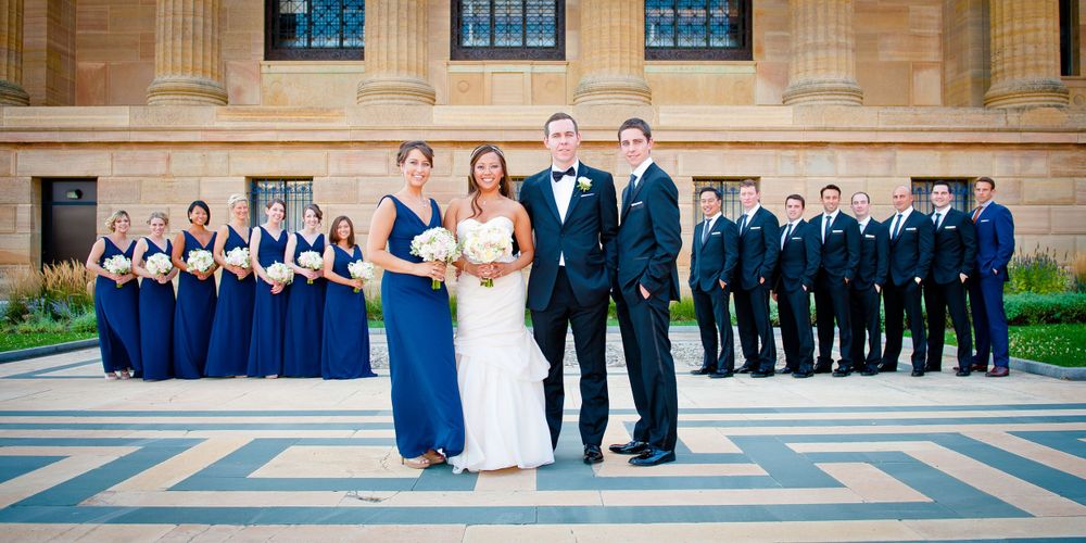 Wedding party in blue and black formal attire posed on grand stone steps.