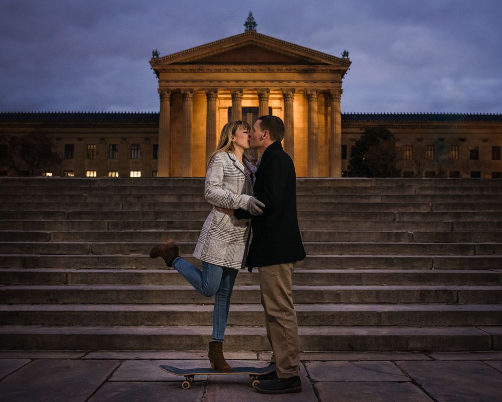 Romantic couple embracing on illuminated museum steps at dusk.