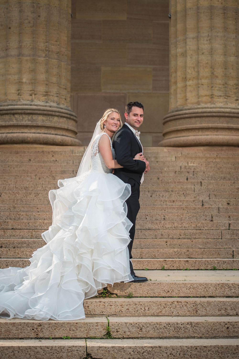 Wedding portrait on grand stone steps between classical columns.