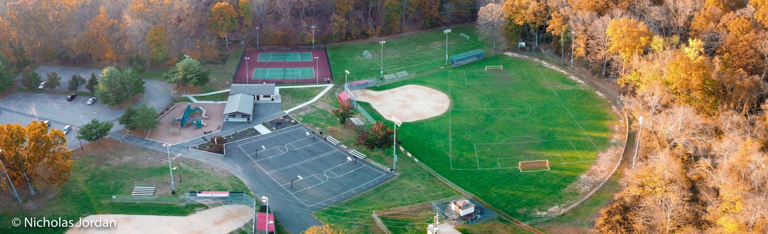 Drone shot of sports fields and buildings surrounded by vibrant fall trees.