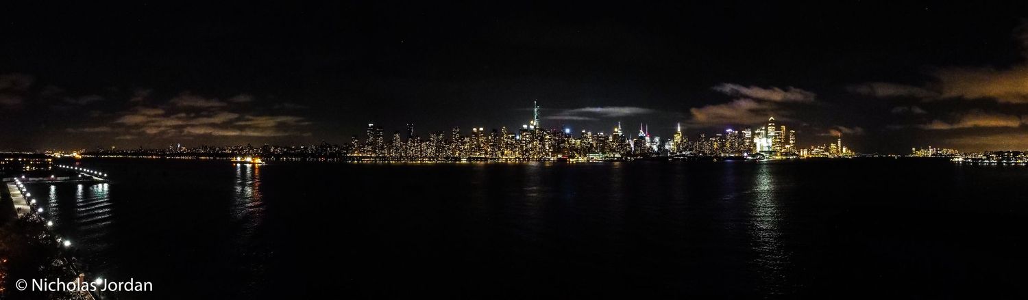 Night cityscape showing illuminated buildings and waterfront reflections.
