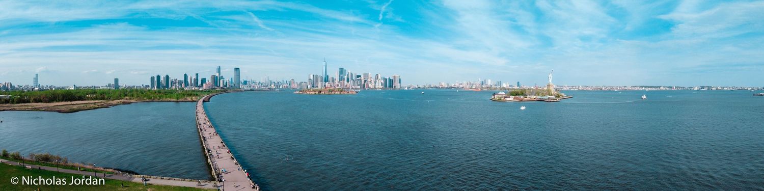 Panoramic aerial view of harbor with city skyline and boats on blue water.