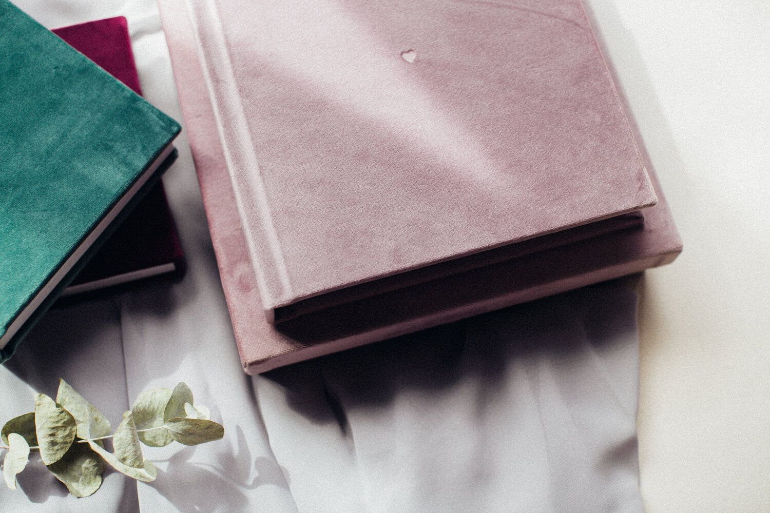 Elegant velvet photo albums in green, burgundy and blush pink with decorative elements.