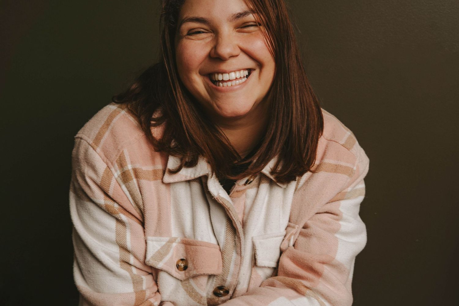 Portrait of someone in beige jacket laughing against dark background.