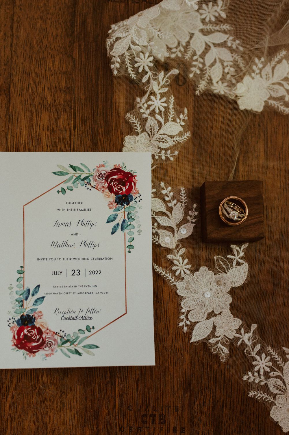 Elegant wedding invitations with floral designs and red roses on a wooden background.