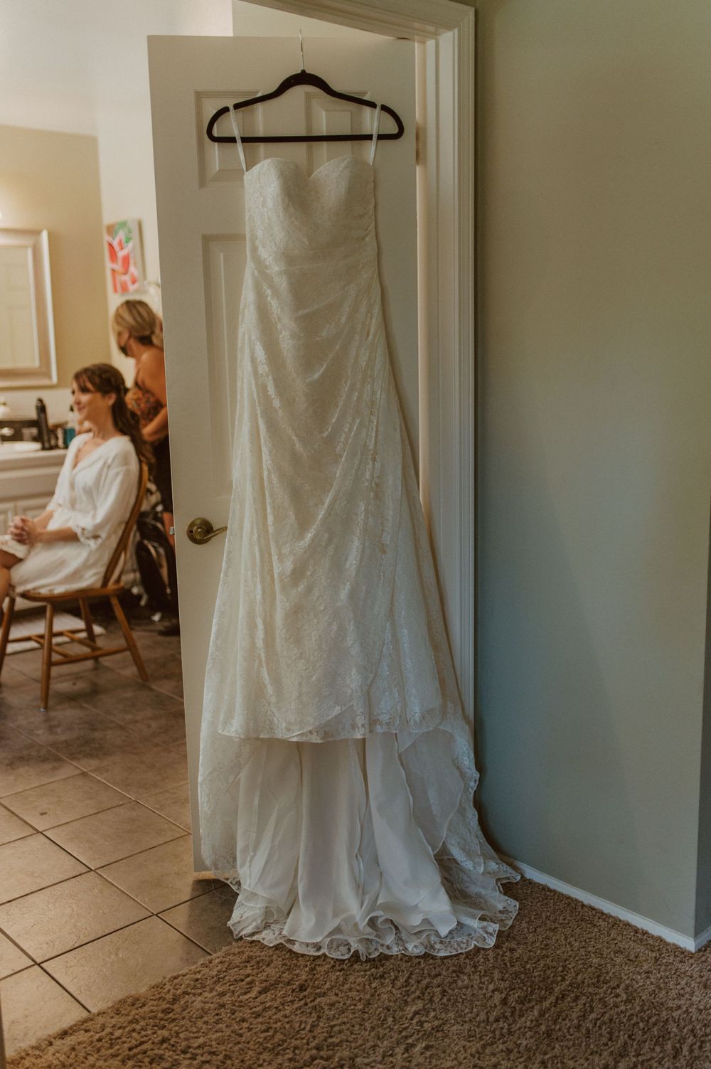 Wedding dress displayed in doorway with preparation scene visible in background.