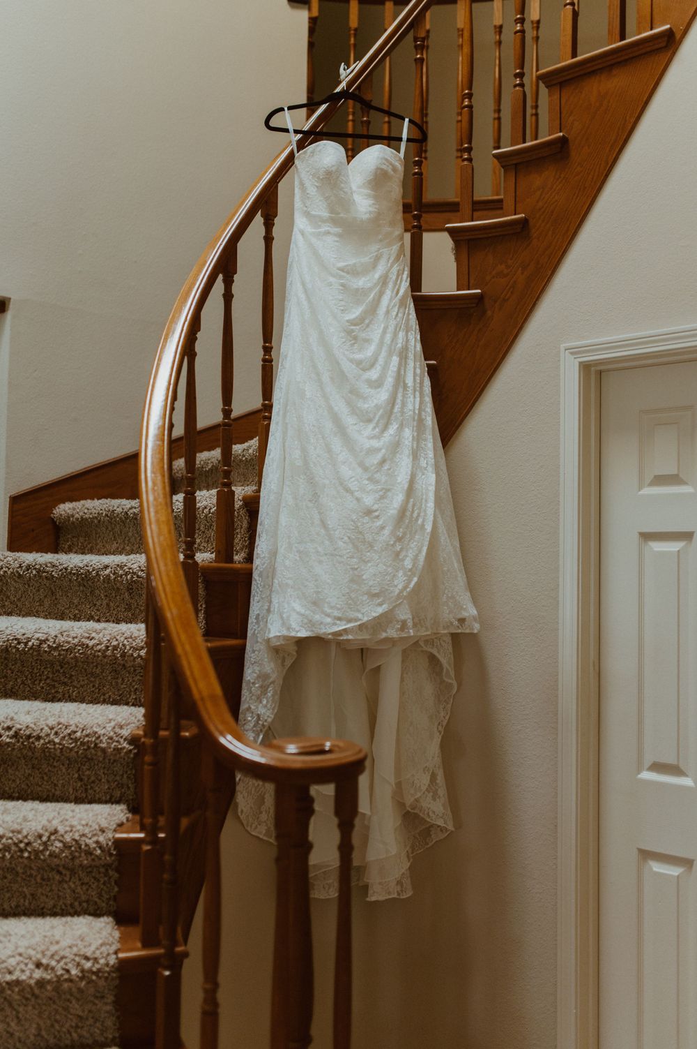 White lace wedding dress hanging on wooden staircase banister.