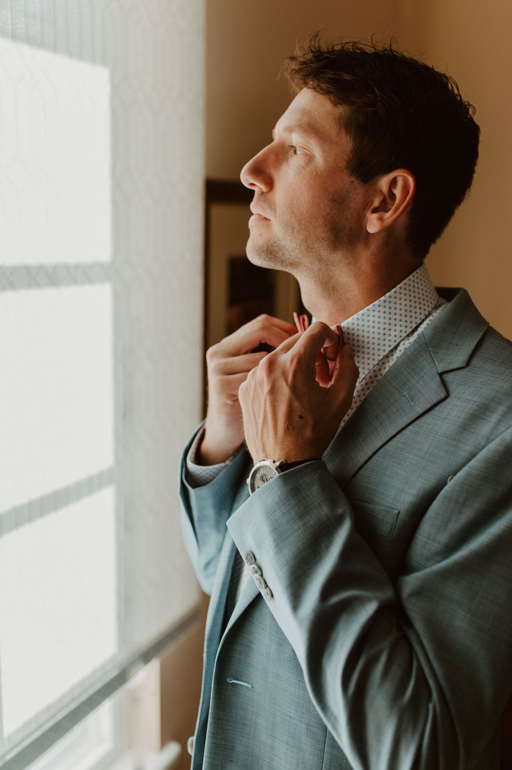 Person in business attire gazes upward near a window in a contemplative pose.