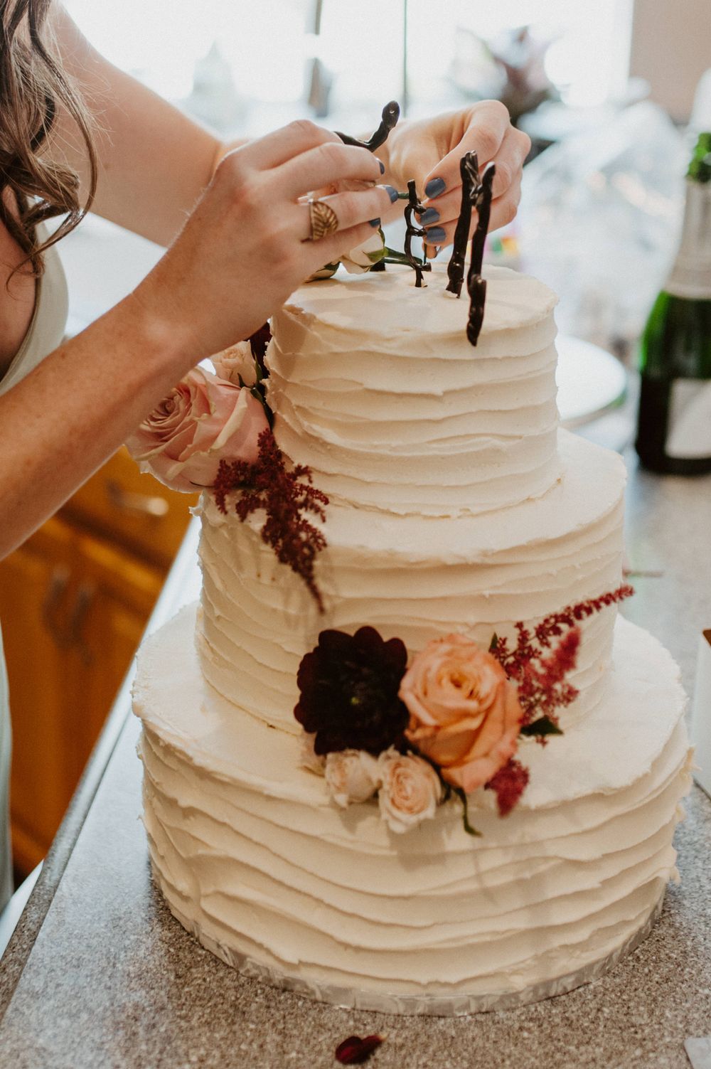 White wedding cake decorated with delicate pink flowers and burgundy accents.