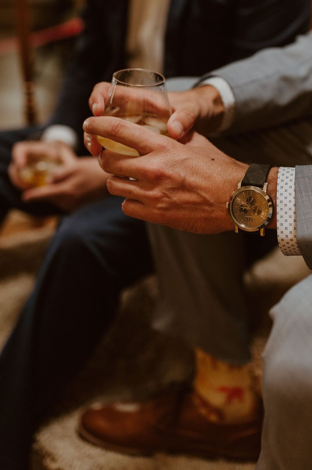 Close-up of hands holding drinks with wedding rings visible in warm lighting.