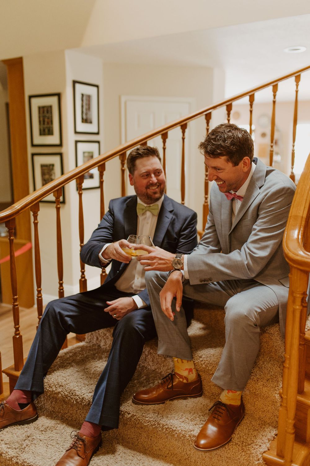 Two people in gray suits share a candid moment while sitting on carpeted stairs.