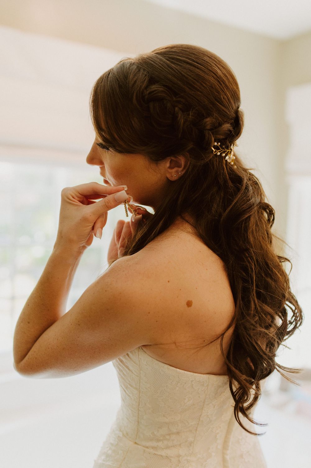 A person in a white dress adjusts their earrings while getting ready.