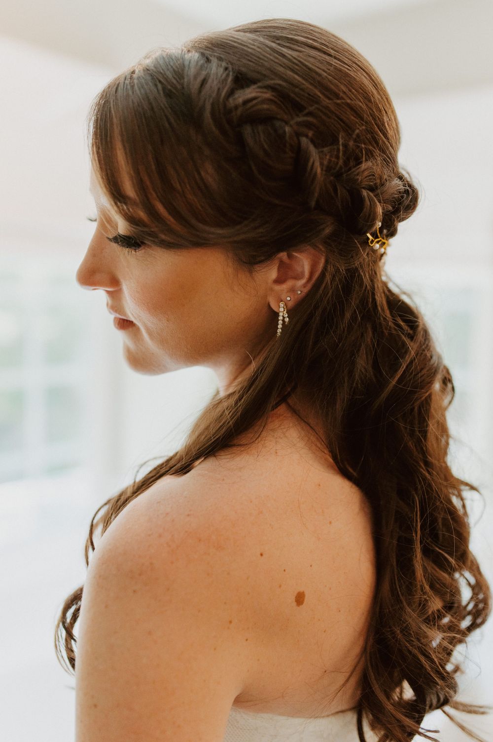 Side profile of elegant bridal hairstyle with soft curls and braided details.