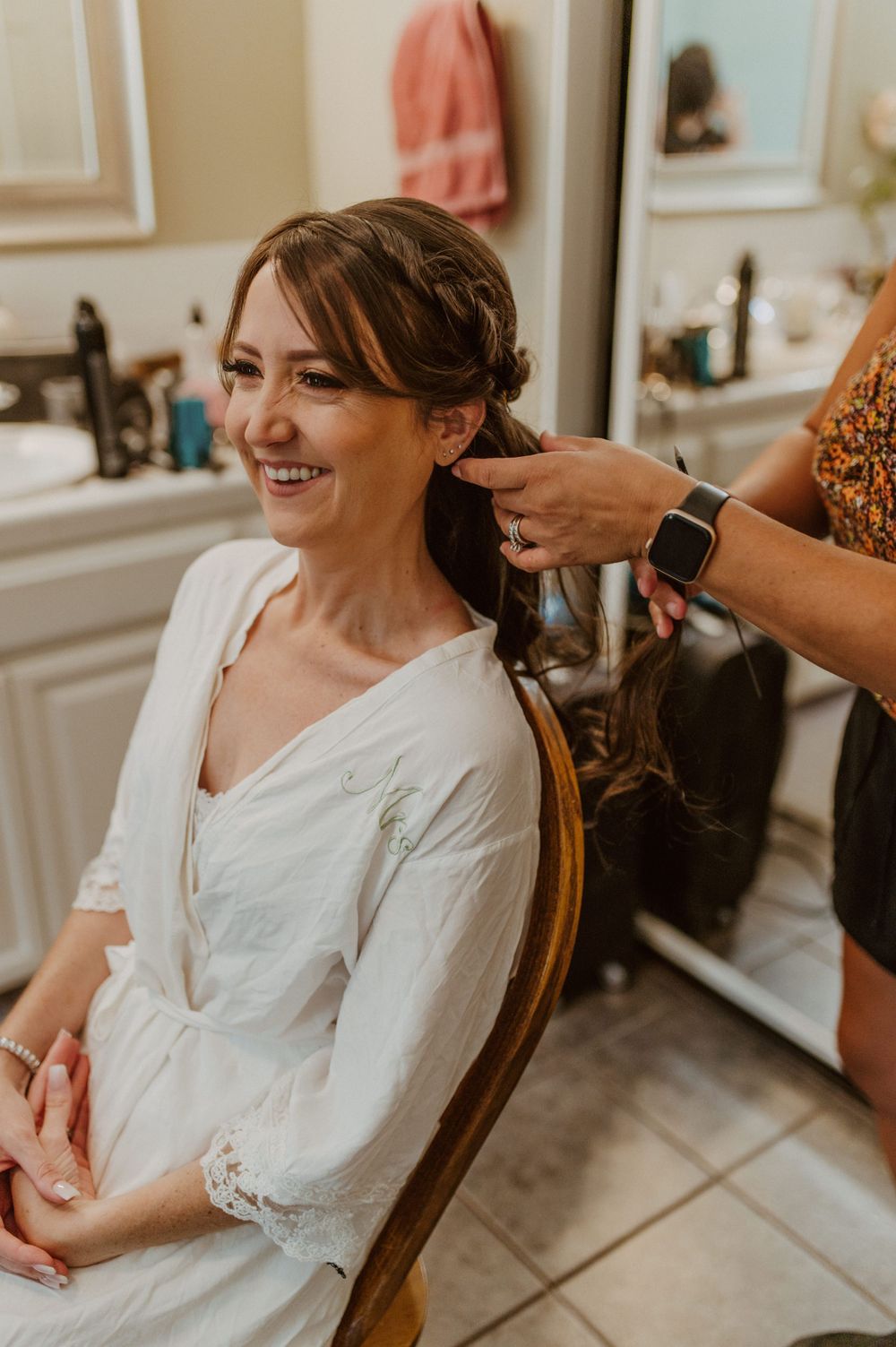 A person in white gets their hair styled while sitting in a wooden chair.