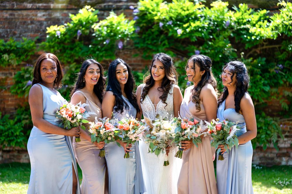 Bride with bridesmaids at Hatfield House by Foto Collective, holding spring bouquets in pale blue dresses in the sunny garden grounds.