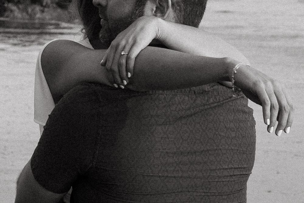 A black and white photograph shows a close-up view of an intimate embrace between two people.
