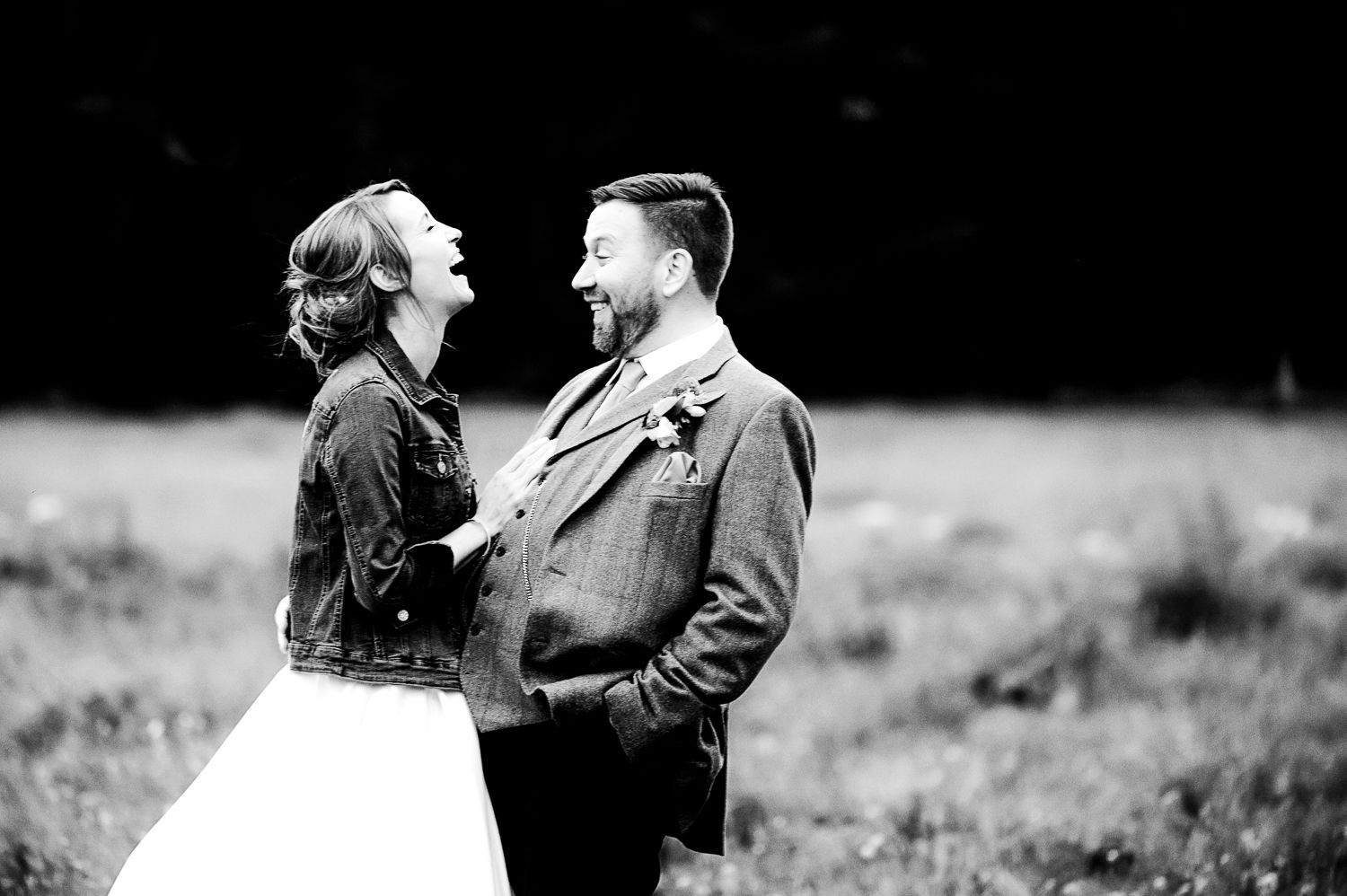 A black and white wedding portrait captures a joyful moment between a couple in a field.