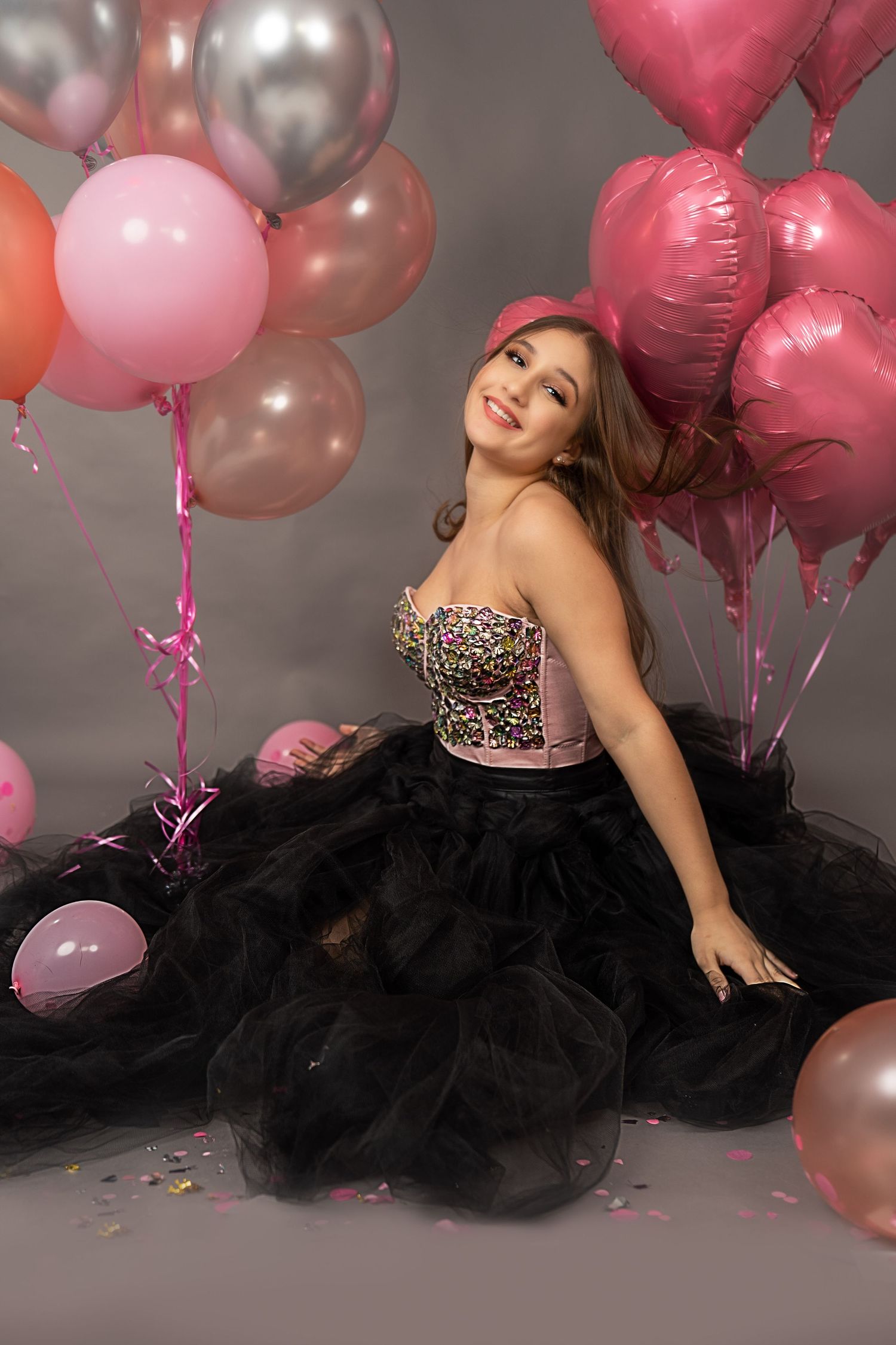 Portrait of person in black tulle gown surrounded by pink and silver balloons.