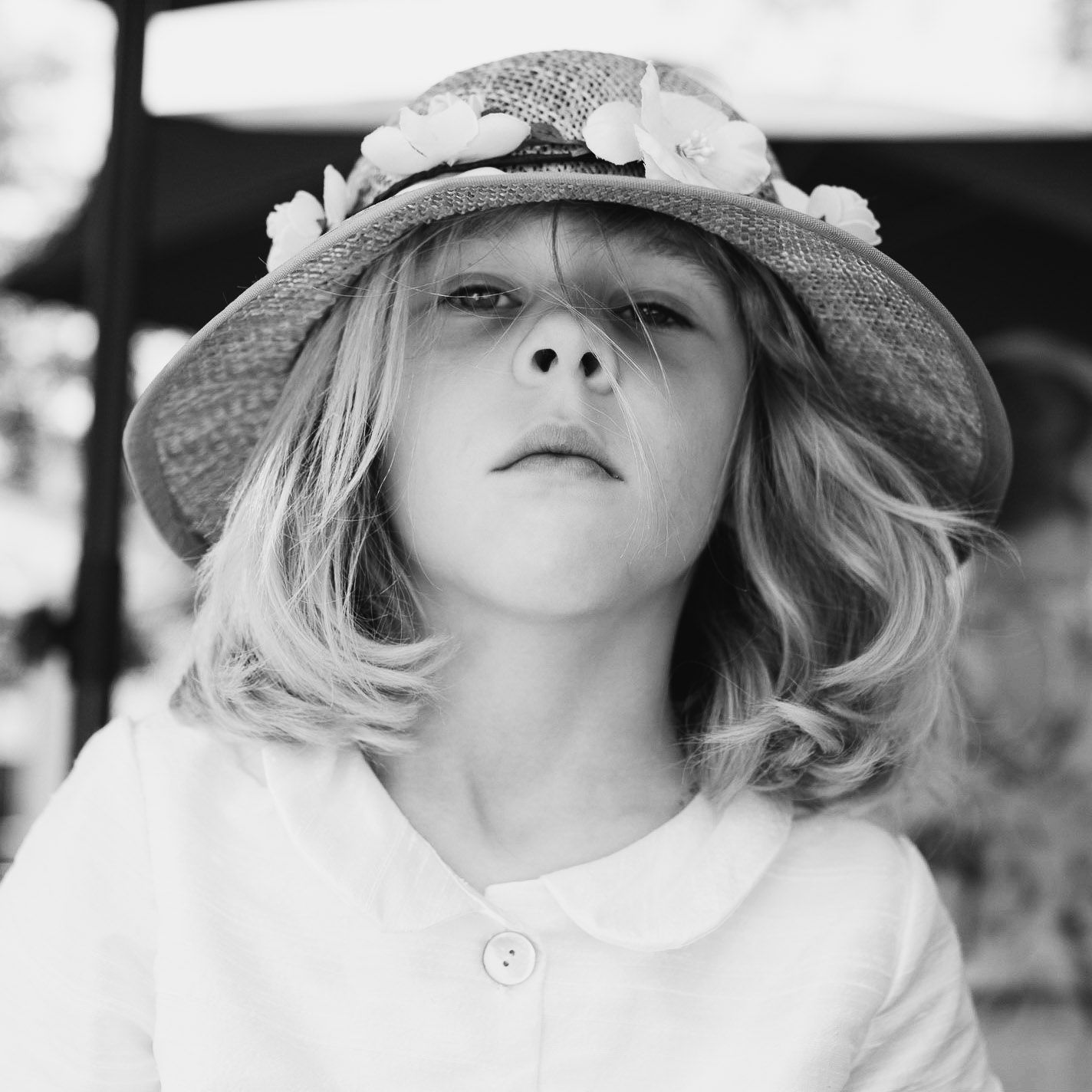 Portrait of a child wearing a floral-decorated sun hat looking upward with a whimsical expression.