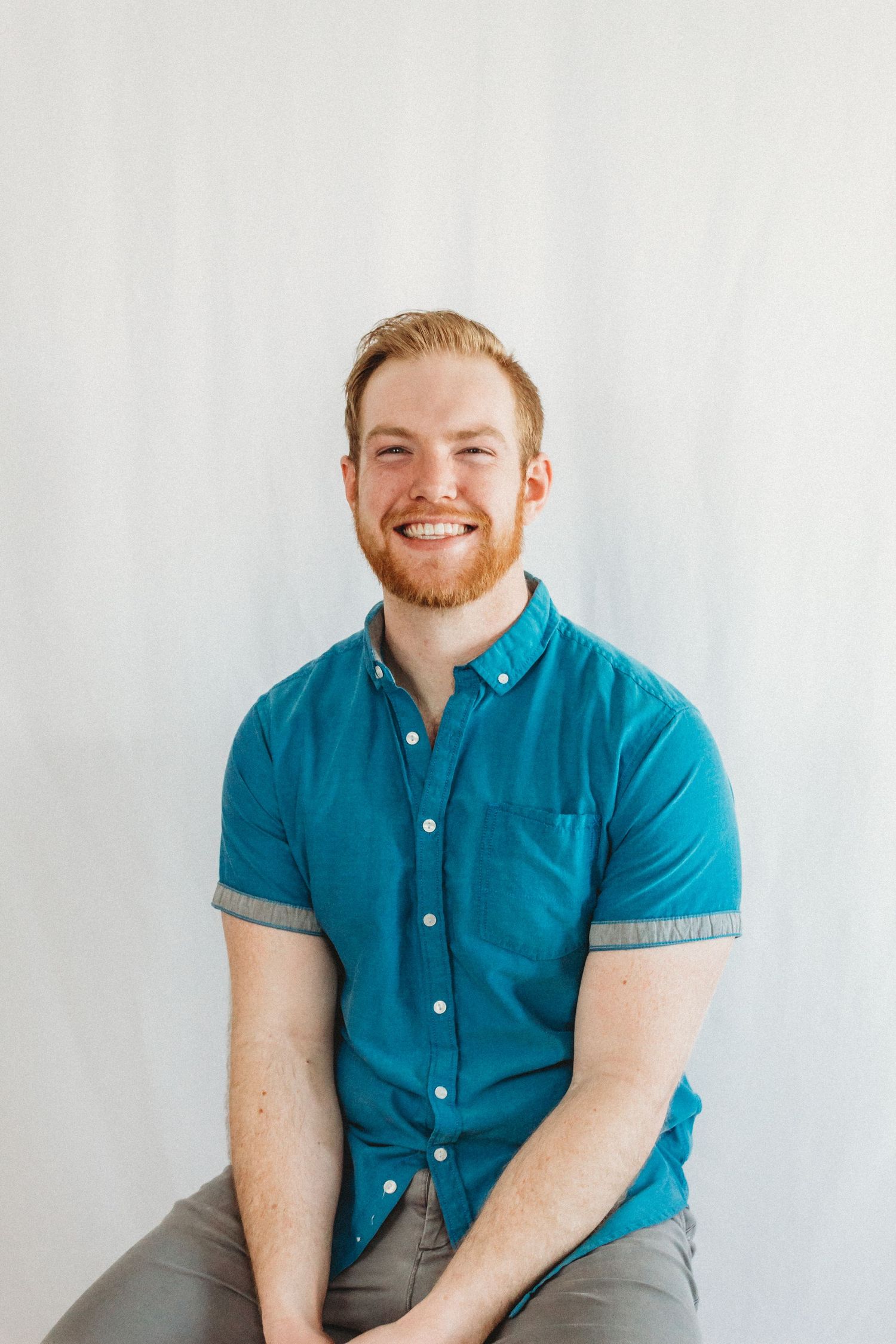 Portrait of someone in a bright teal button-down shirt against a white background.