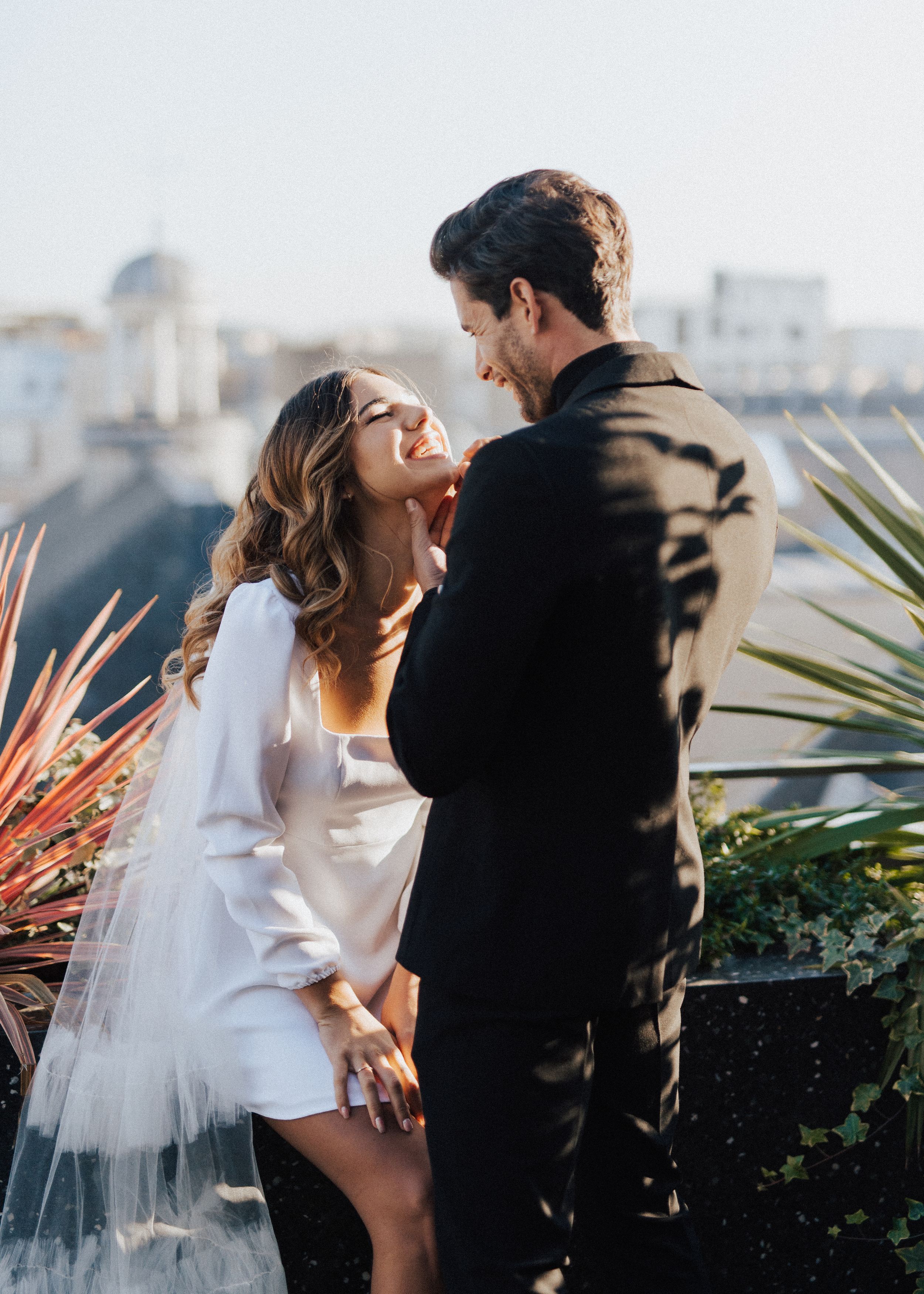 Romantic rooftop wedding portraits with urban skyline and tropical plants.