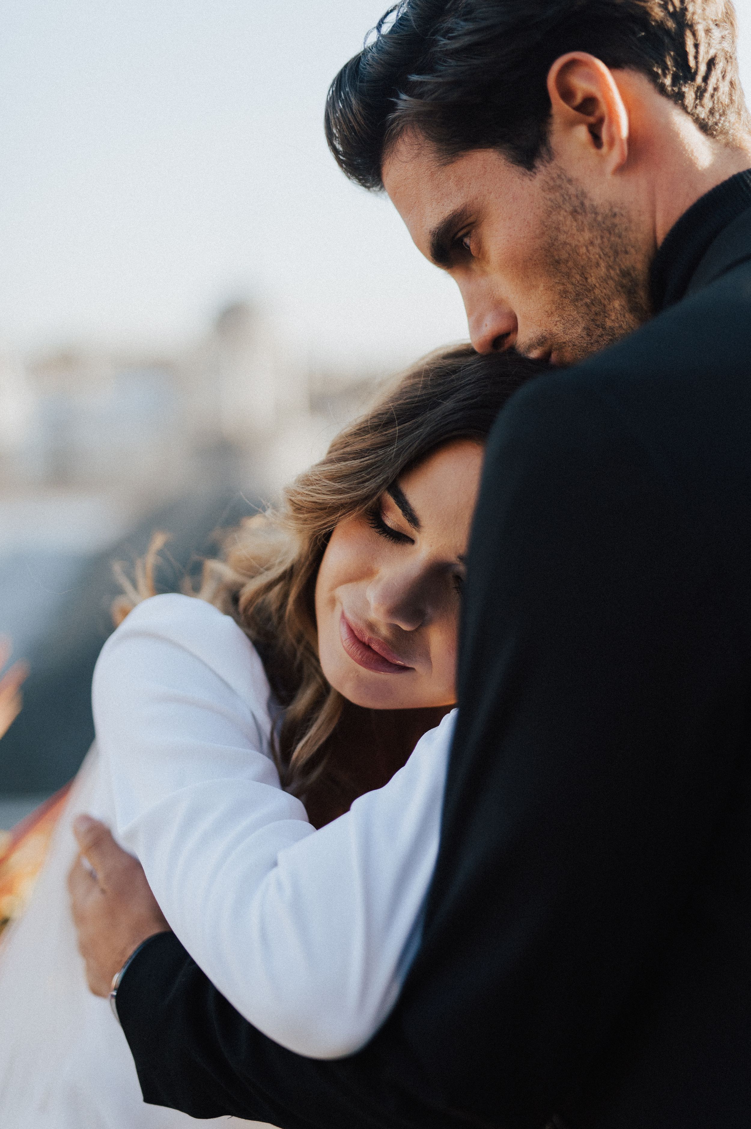 Intimate wedding couple embrace against city backdrop during sunset.