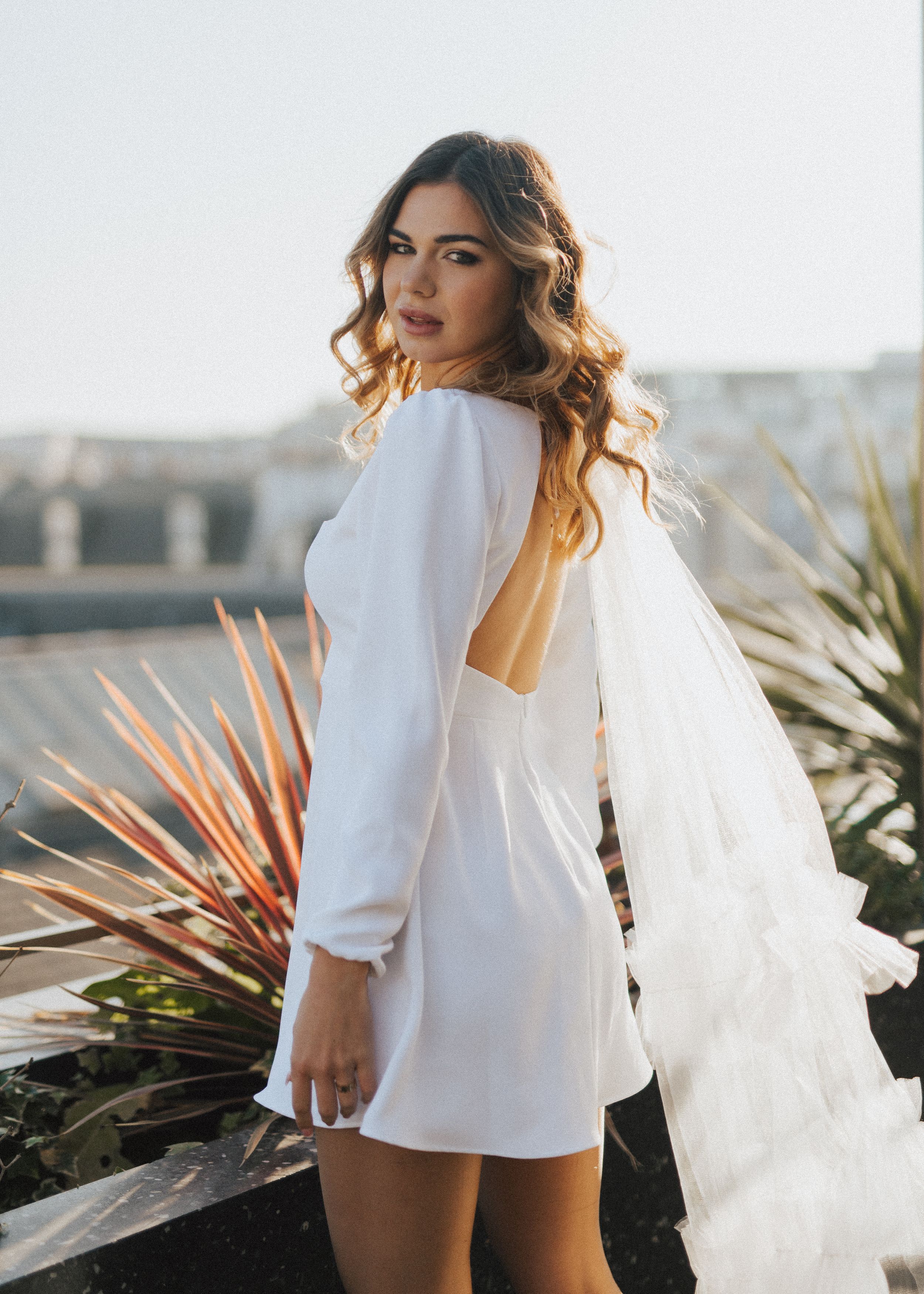 Bridal portrait with flowing veil and tropical plants on urban rooftop.