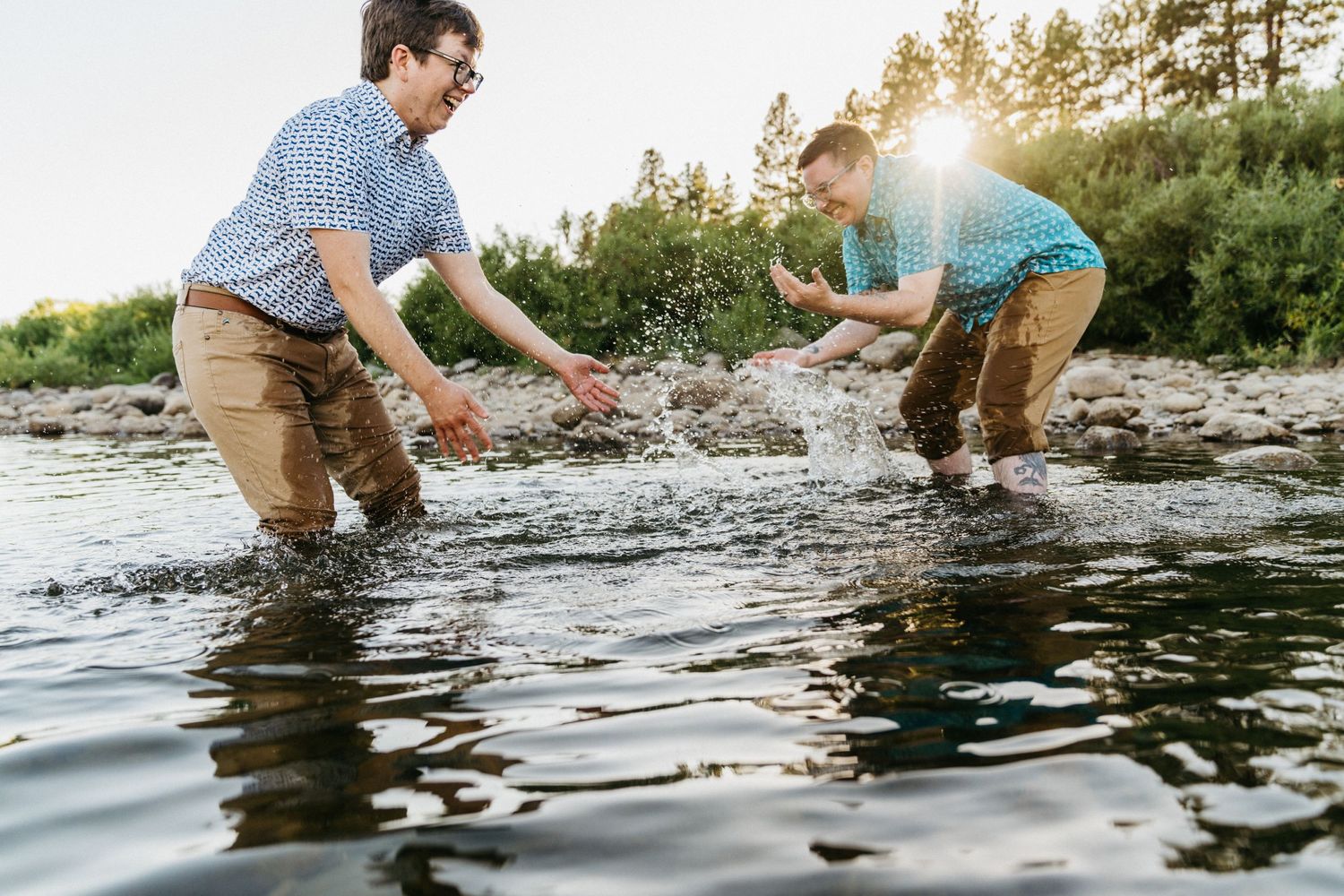 Two people splashing and playing in a lake during golden hour.