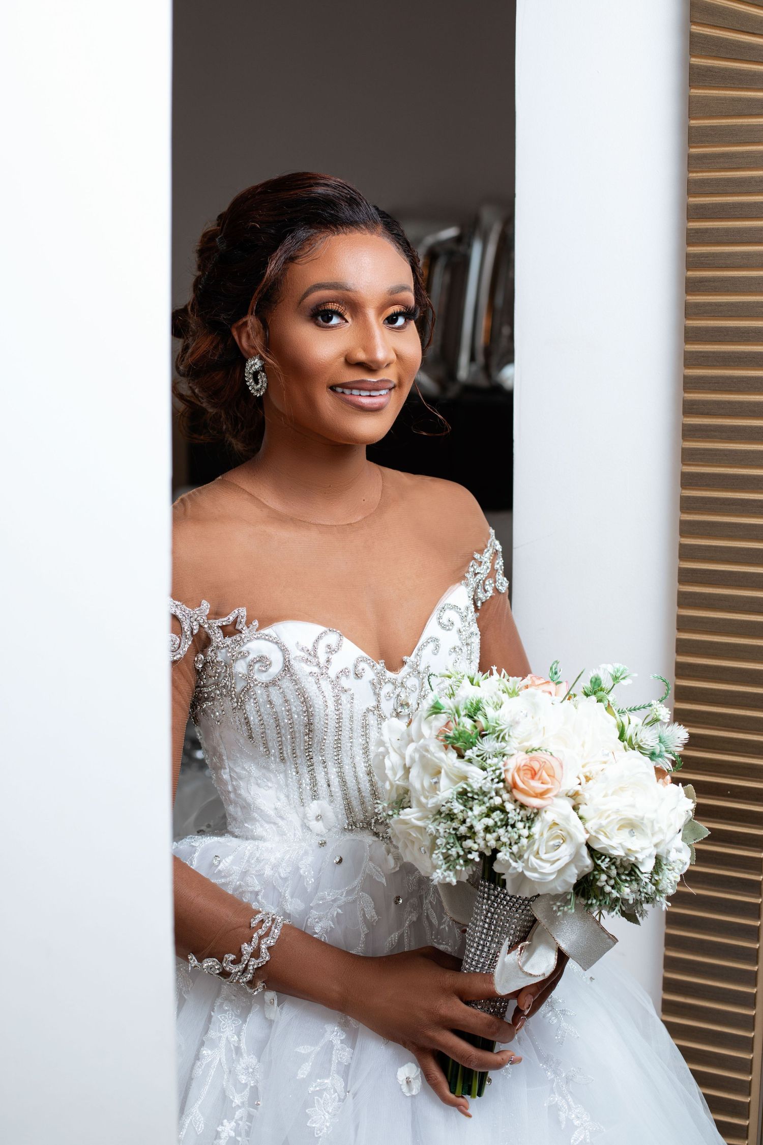 Bride in elegant white lace gown holds bouquet of white flowers.