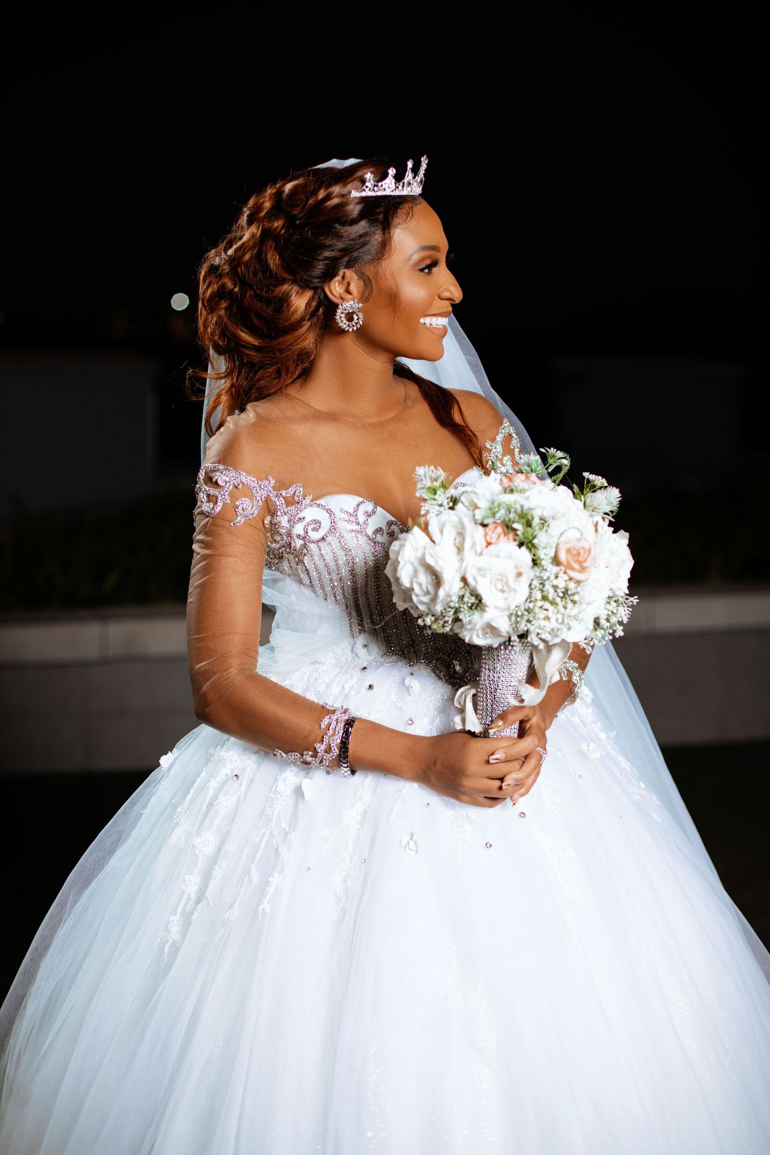Bride in luxurious white ball gown with off-shoulder details holds a white bouquet.
