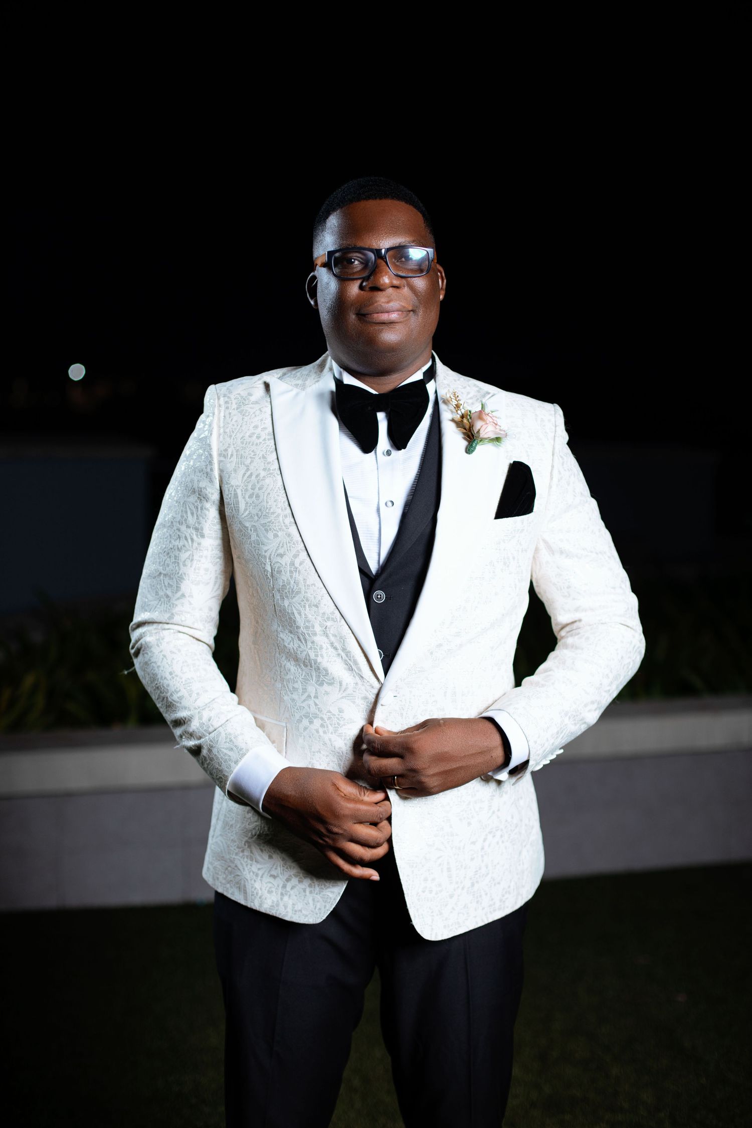 Groom poses in stylish white sequined tuxedo jacket with black bow tie.