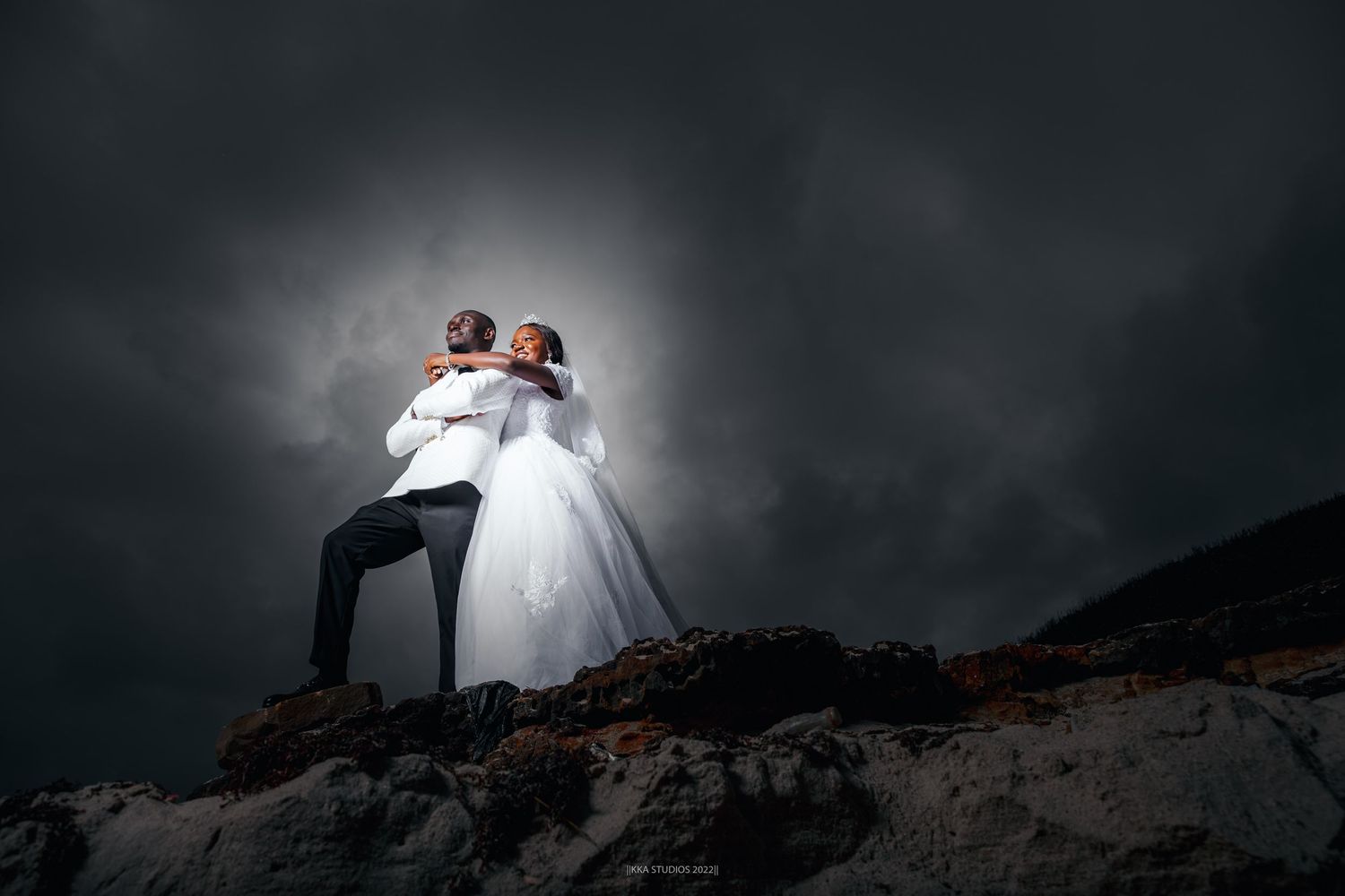 Dramatic moody wedding photo on rocky cliff with stormy sky background.