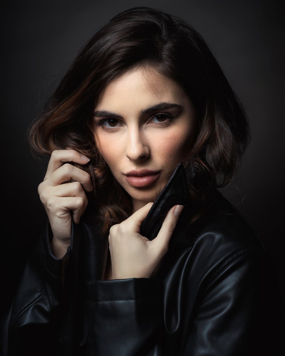 Dark moody portrait with dramatic lighting showing person in black leather against dark background.