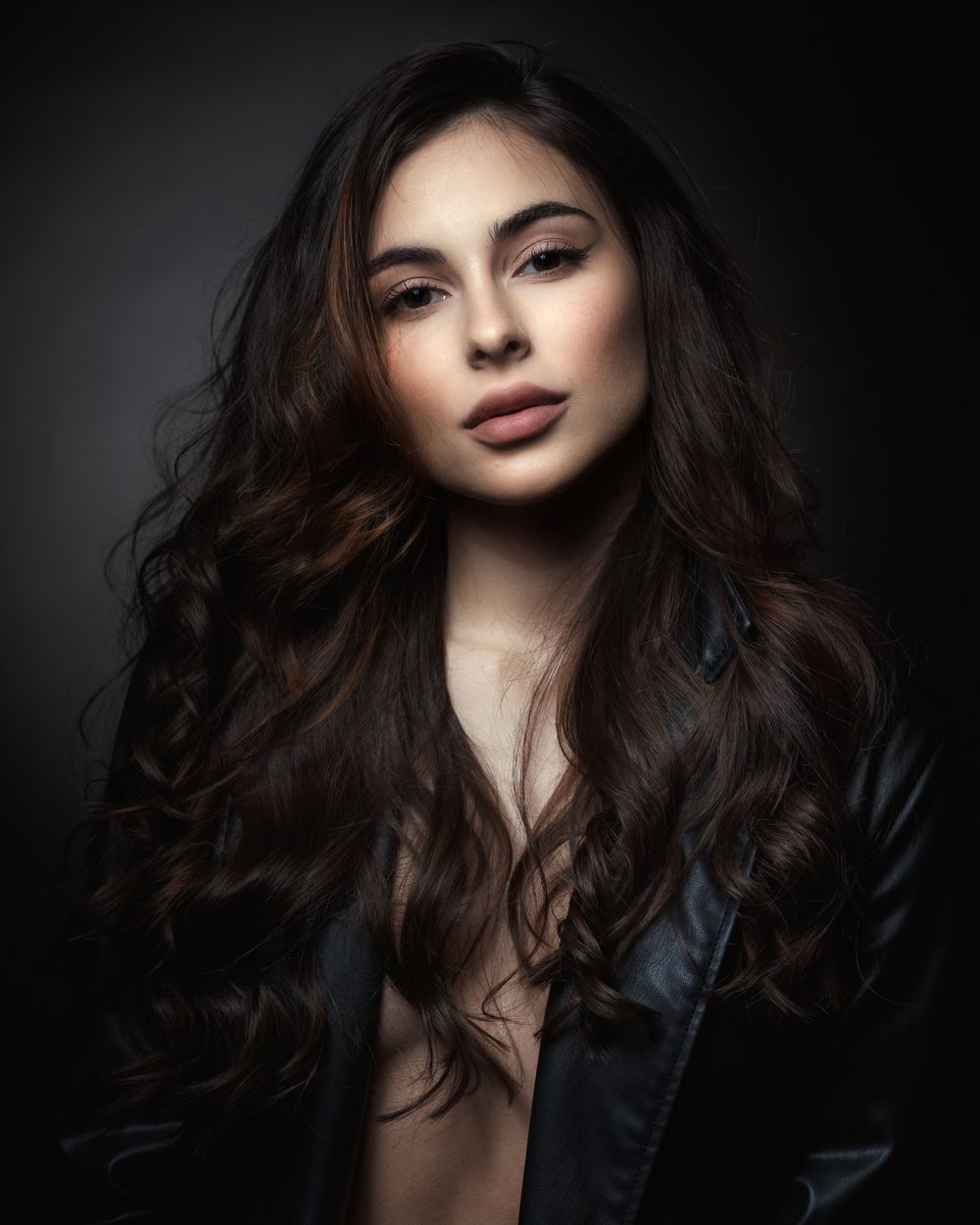 Glamorous beauty shot with flowing brunette waves and dark fashion styling.