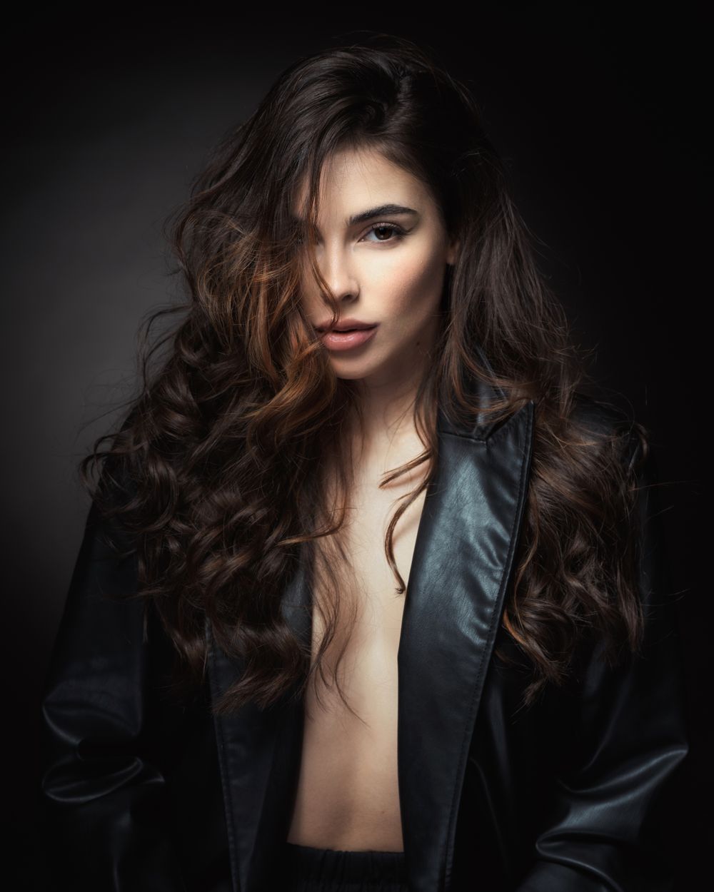 Dramatic fashion portrait with tousled hair and leather jacket in moody lighting.