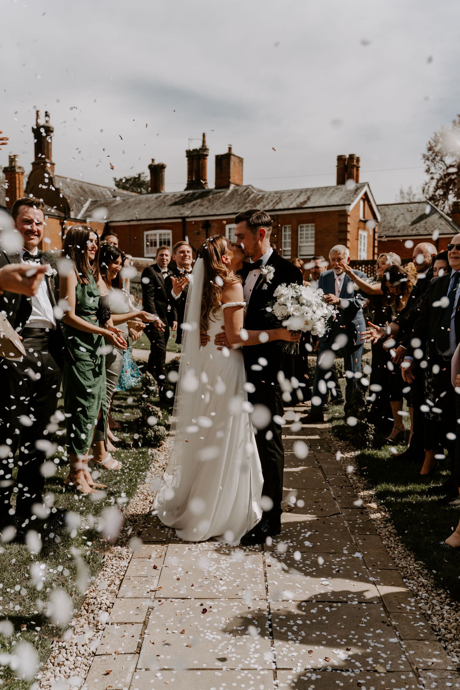 a couple standing kissing while their guests throw white confetti over them