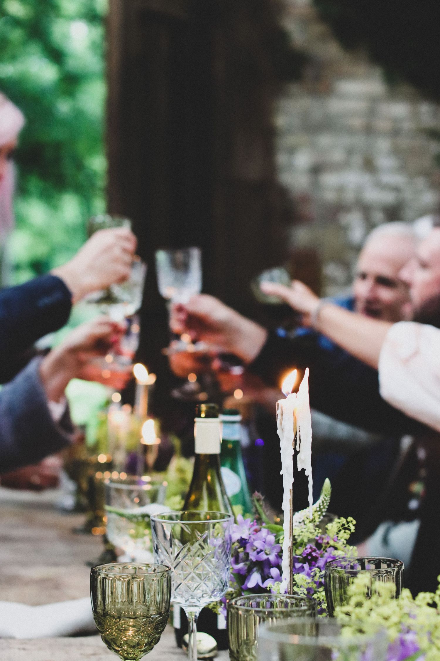Friends toasting with wine glasses over candlelit outdoor dinner table.
