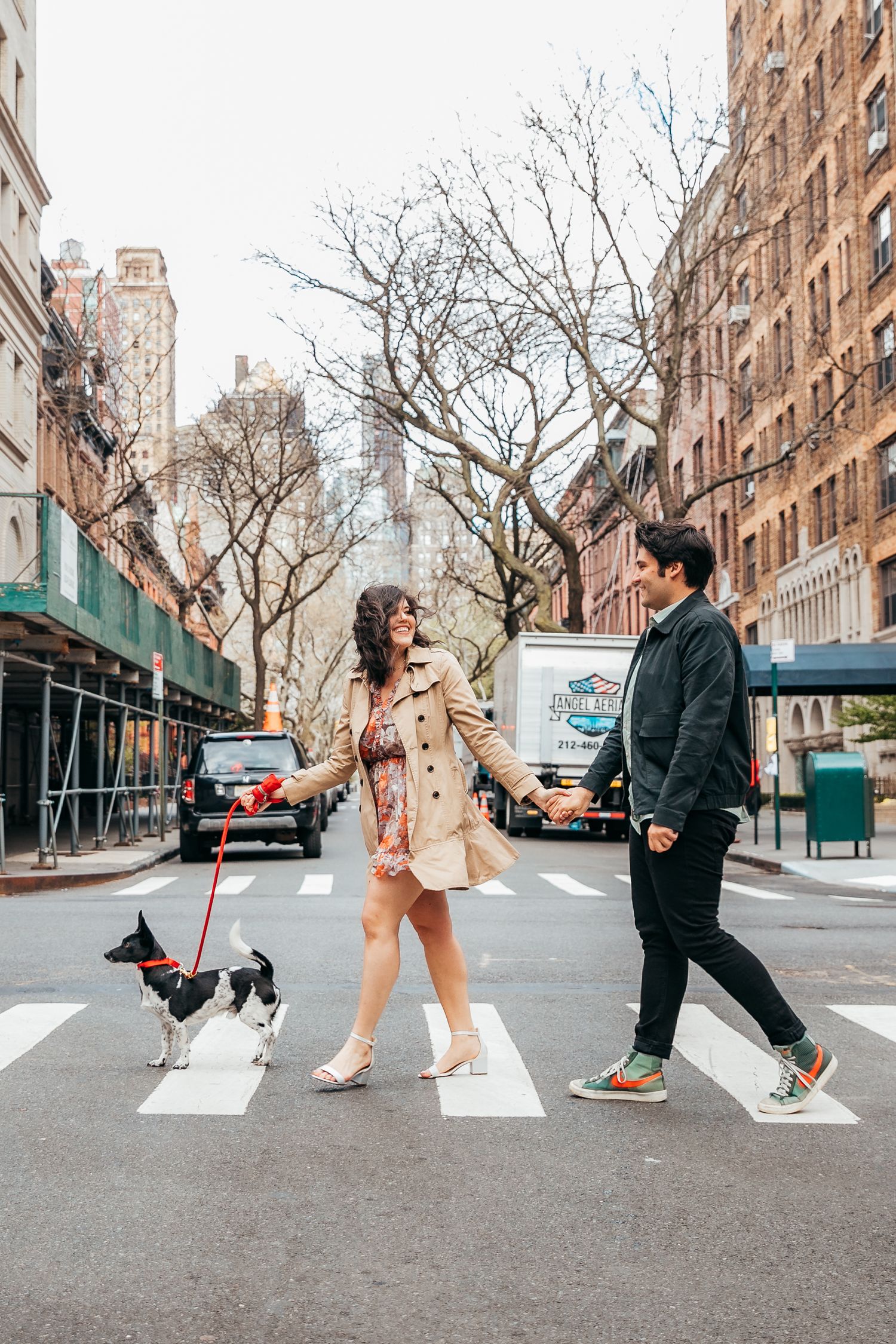 Couple holding hands crossing NYC crosswalk with small black and white dog on leash.