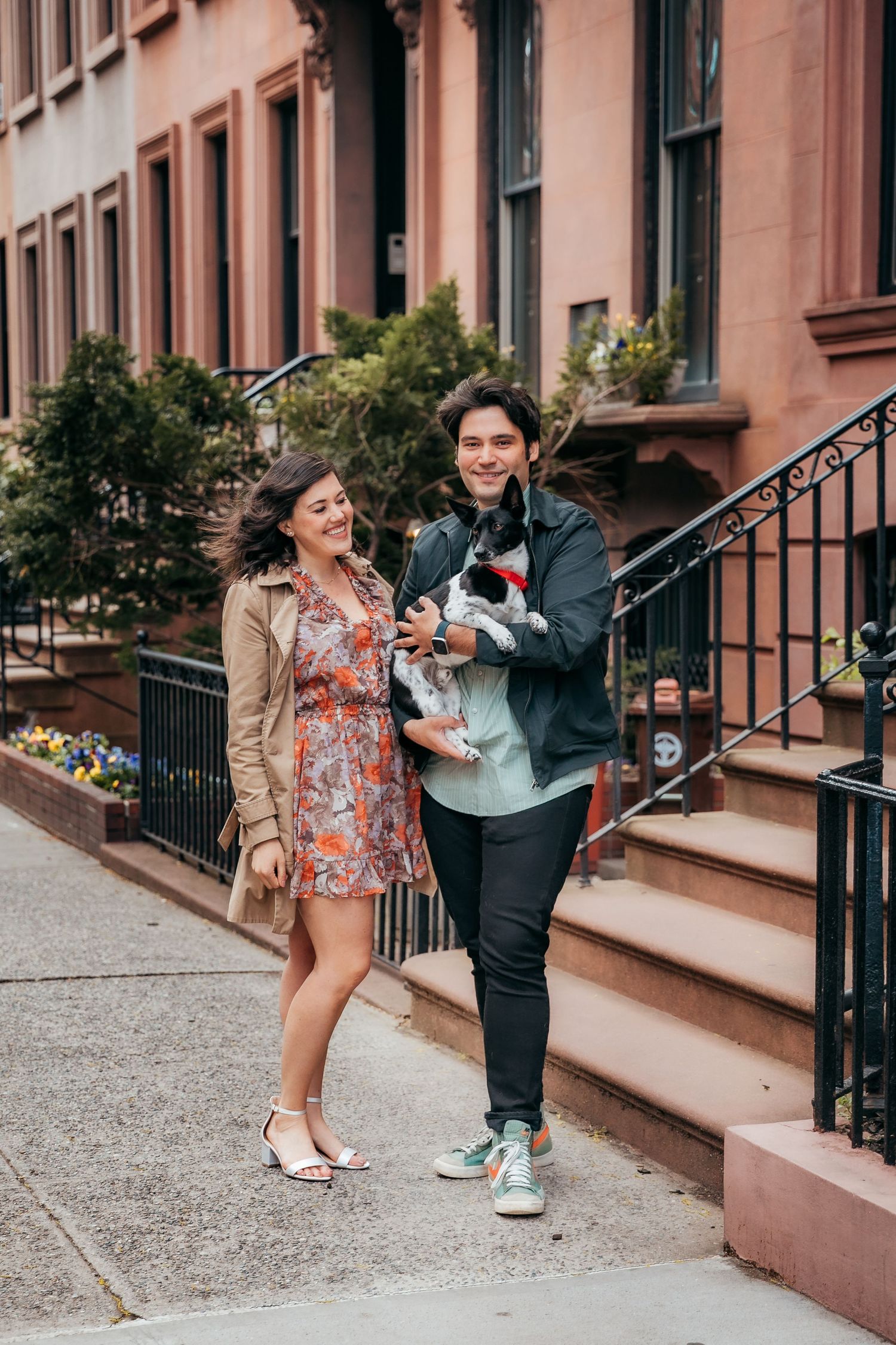 Happy couple walking on NYC sidewalk while man carries small black and white dog.