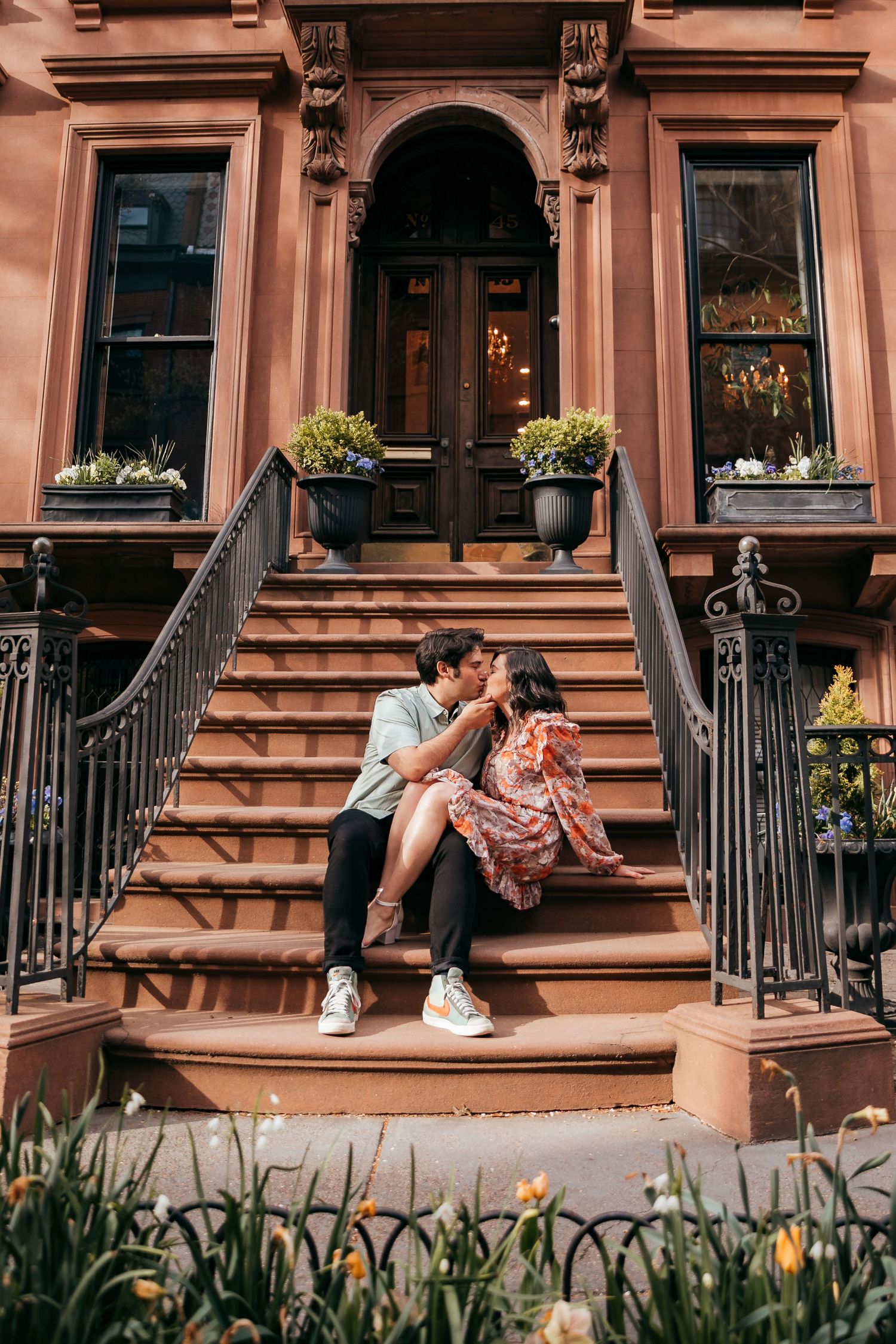 A couple shares a kiss on the steps of a classic NYC brownstone building.