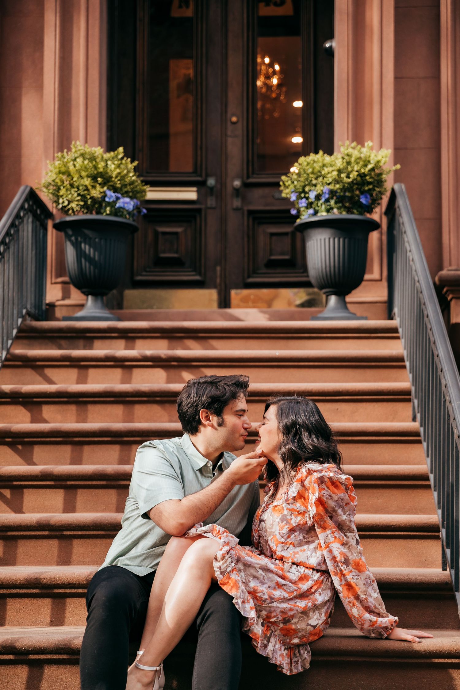 A couple gazes lovingly at each other while sitting on brownstone steps.