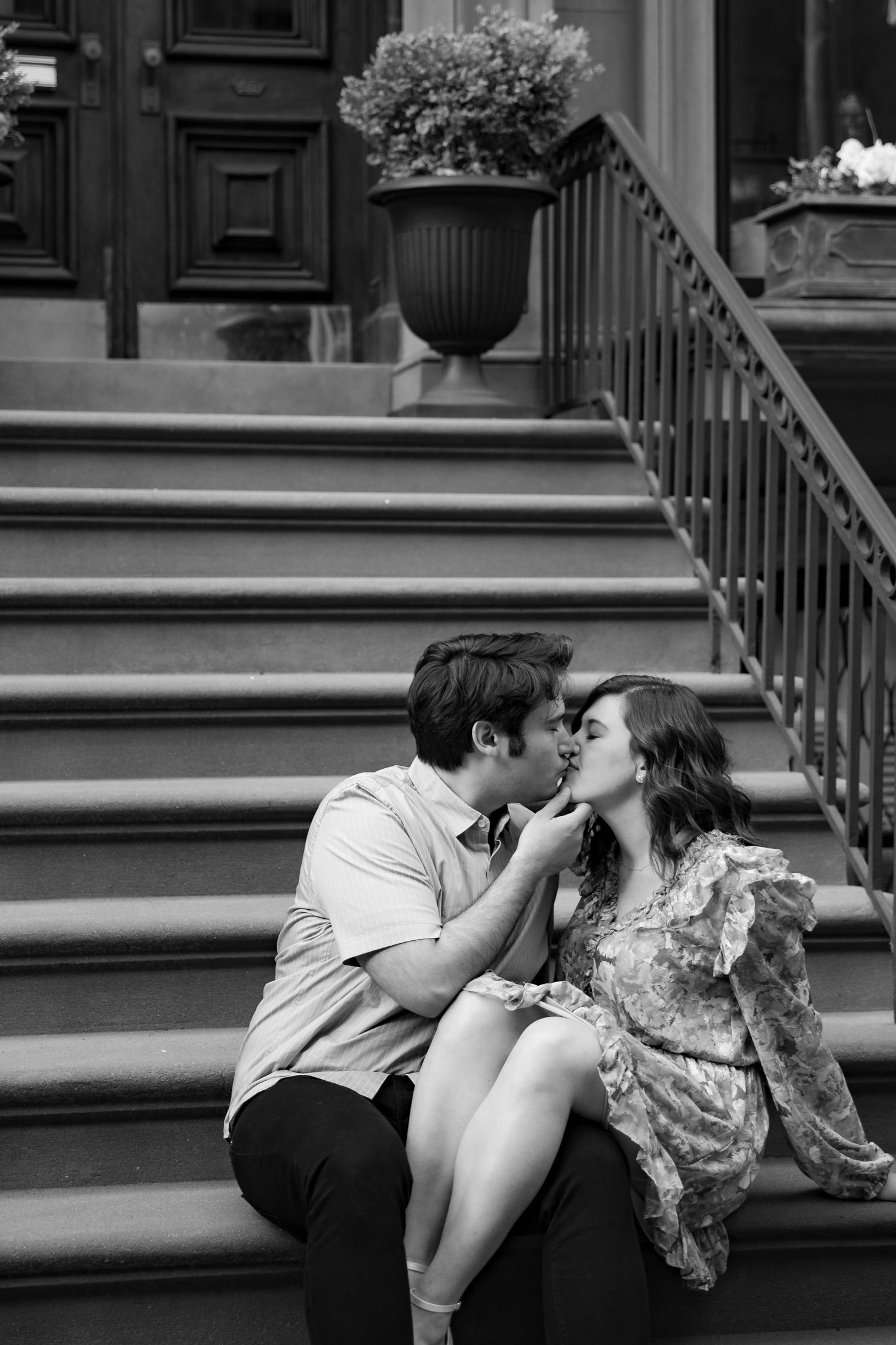 A black and white photo of a couple kissing on brownstone steps.