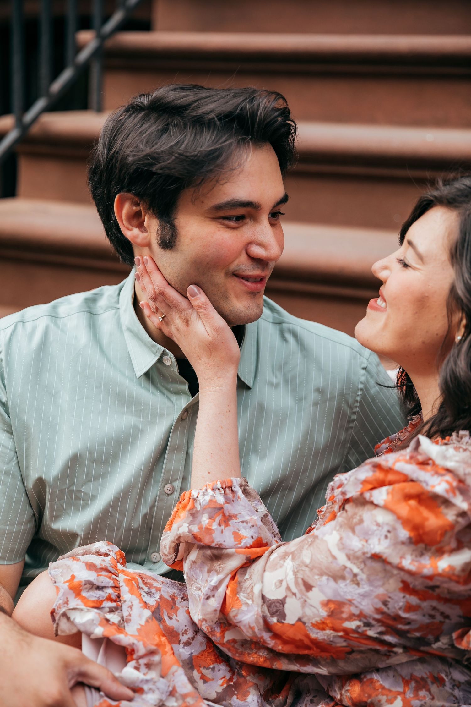 Couple sitting on brownstone steps, woman tenderly touching mans face as they share a romantic moment.